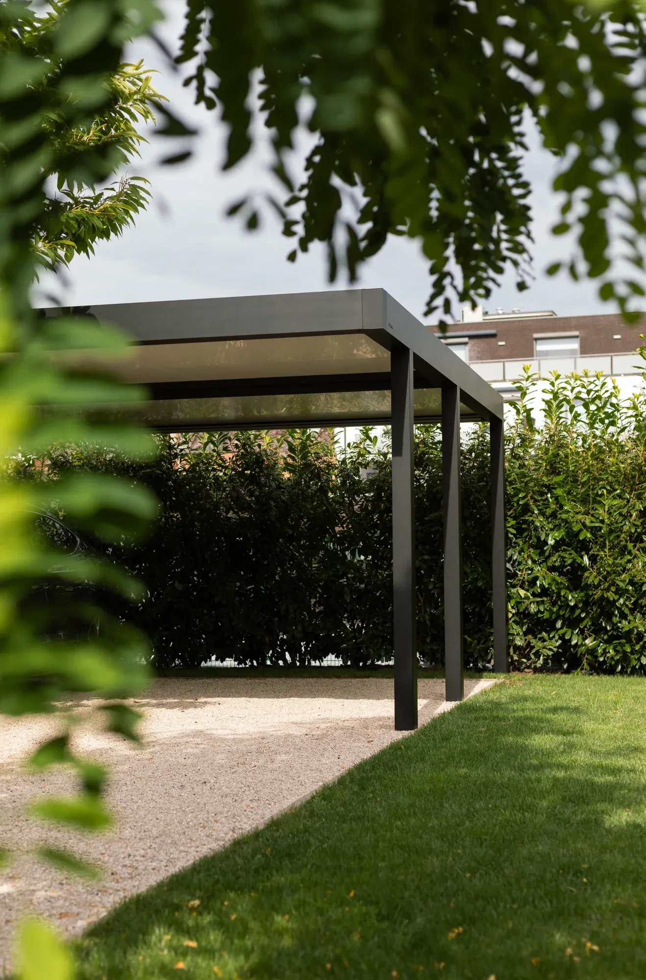 Dunkle Dachkante und schlanke Pfosten eines Aluminium-Carports zwischen Bäumen und Hecken