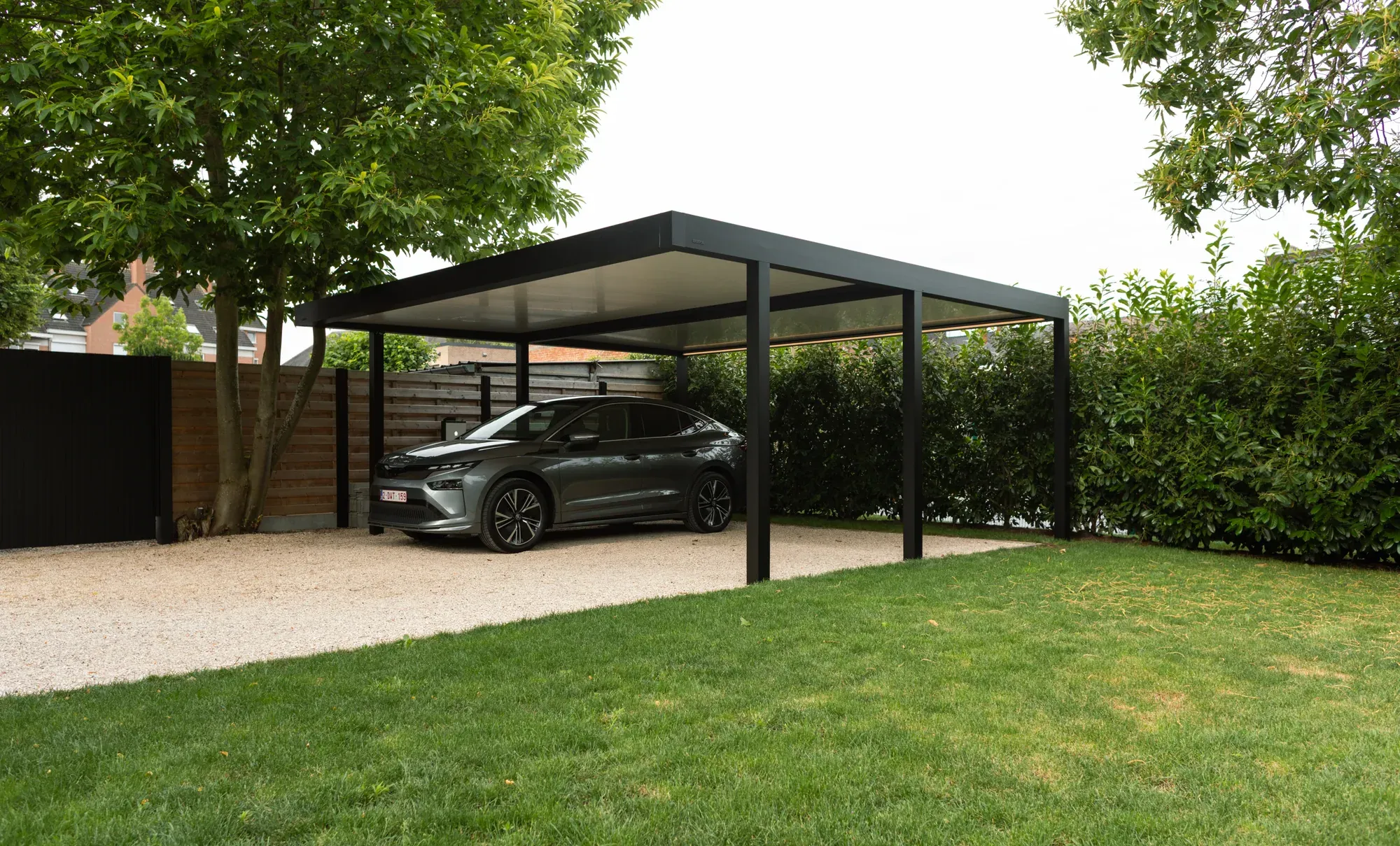 Dunkler Aluminium-Carport mit einem geparkten Auto auf einer Einfahrt neben Rasen und Hecken