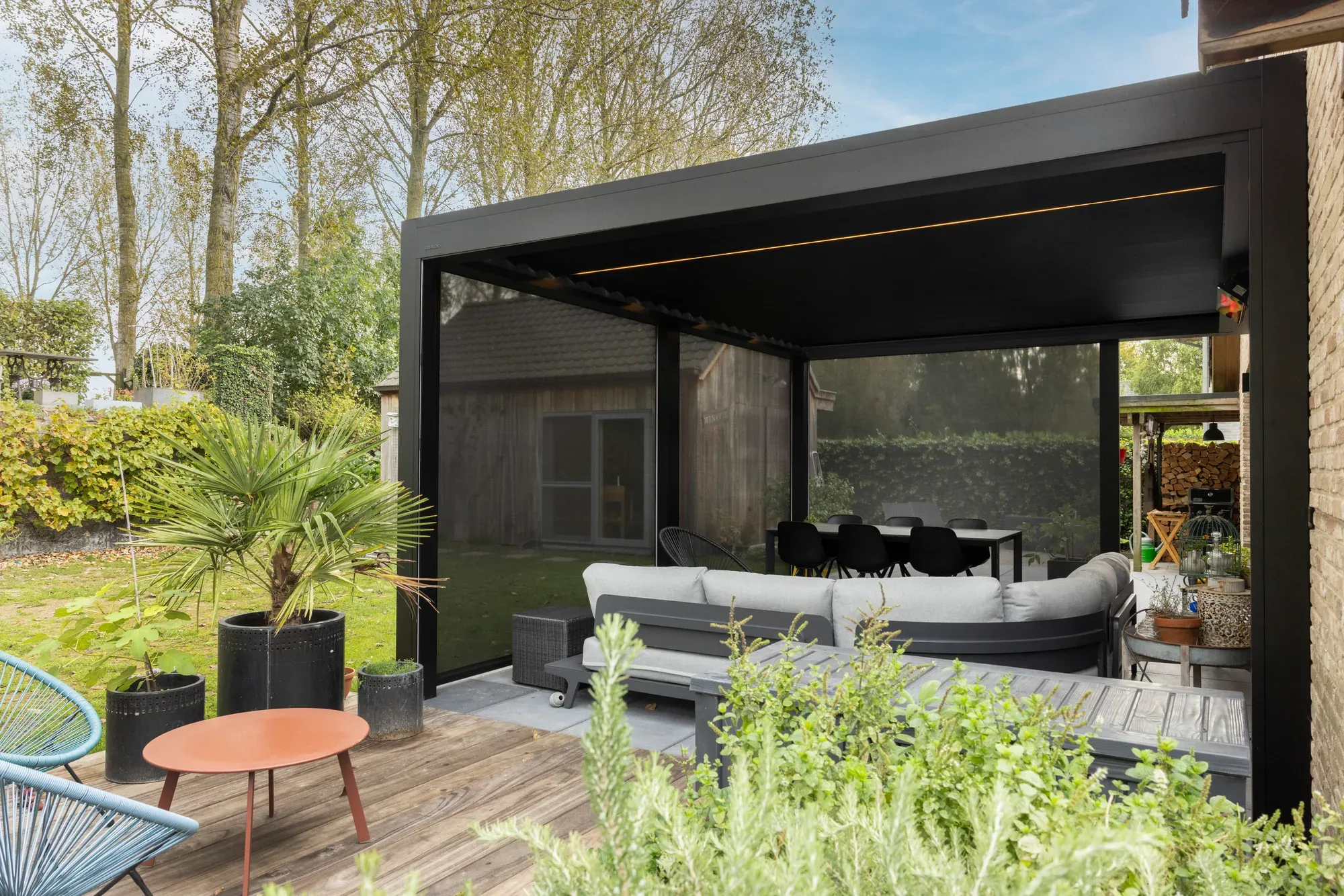 Dunkles Lamellendach mit seitlichem Screen über einer Lounge neben dem Haus