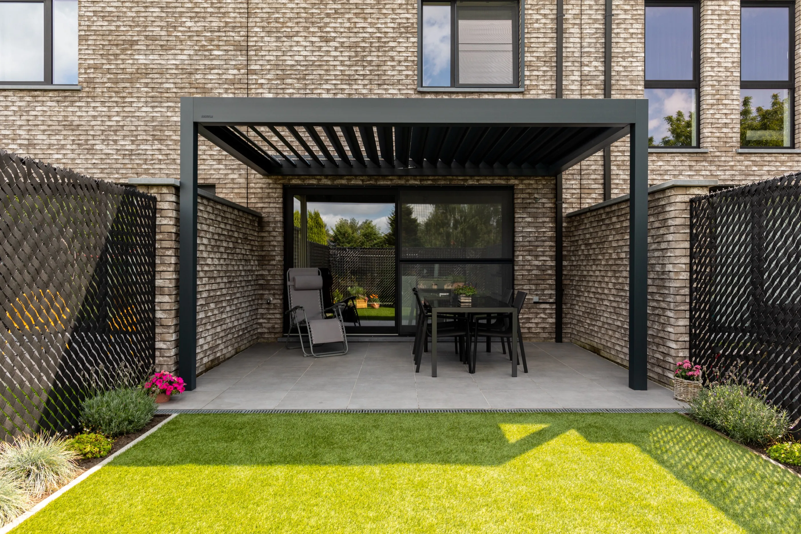 Kompakte überdachte Terrasse vor einer Ziegelfassade mit angrenzendem Garten