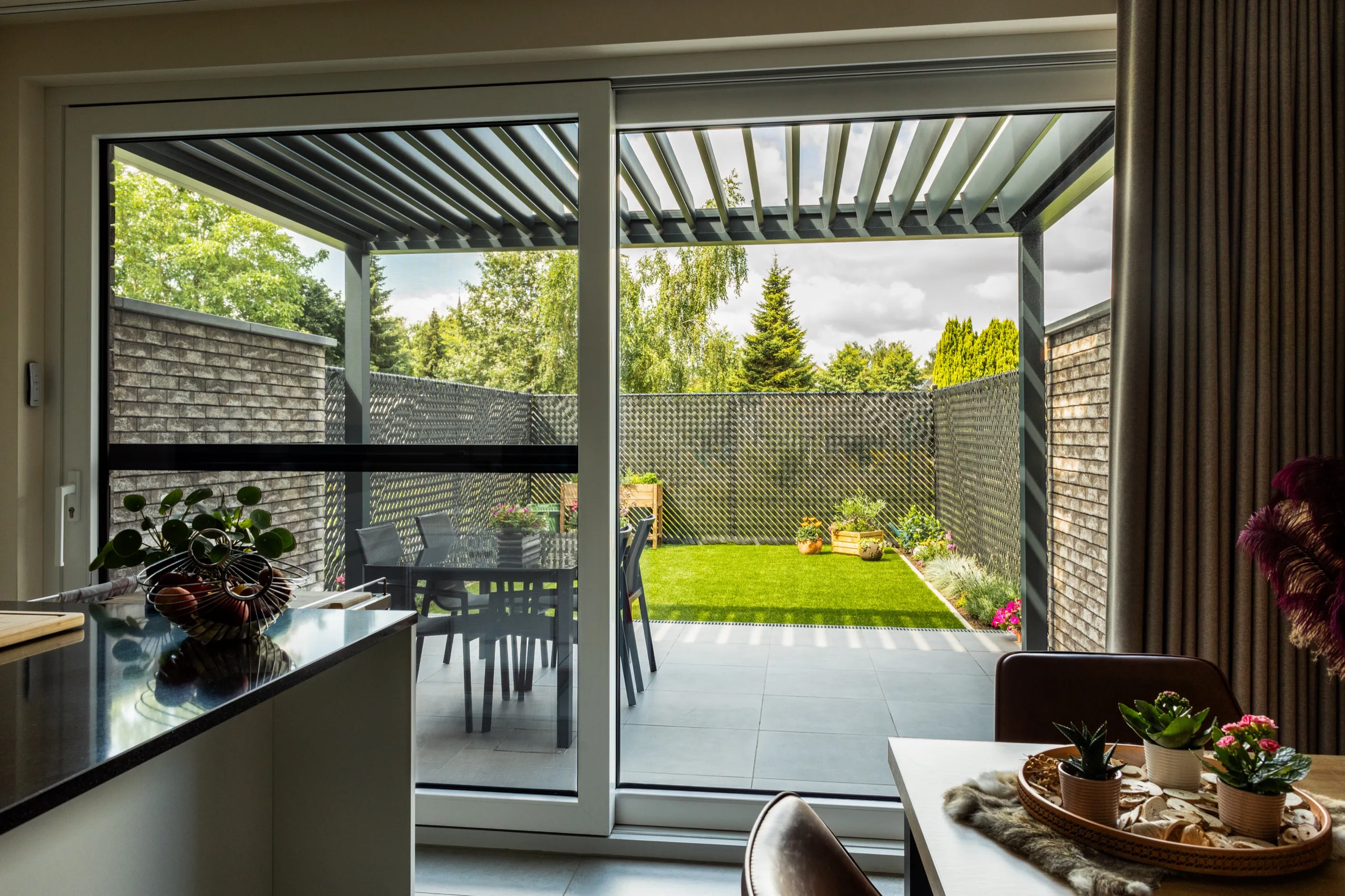 Blick aus dem Wohnraum durch die Terrassentür unter geöffneten Lamellen in den Garten