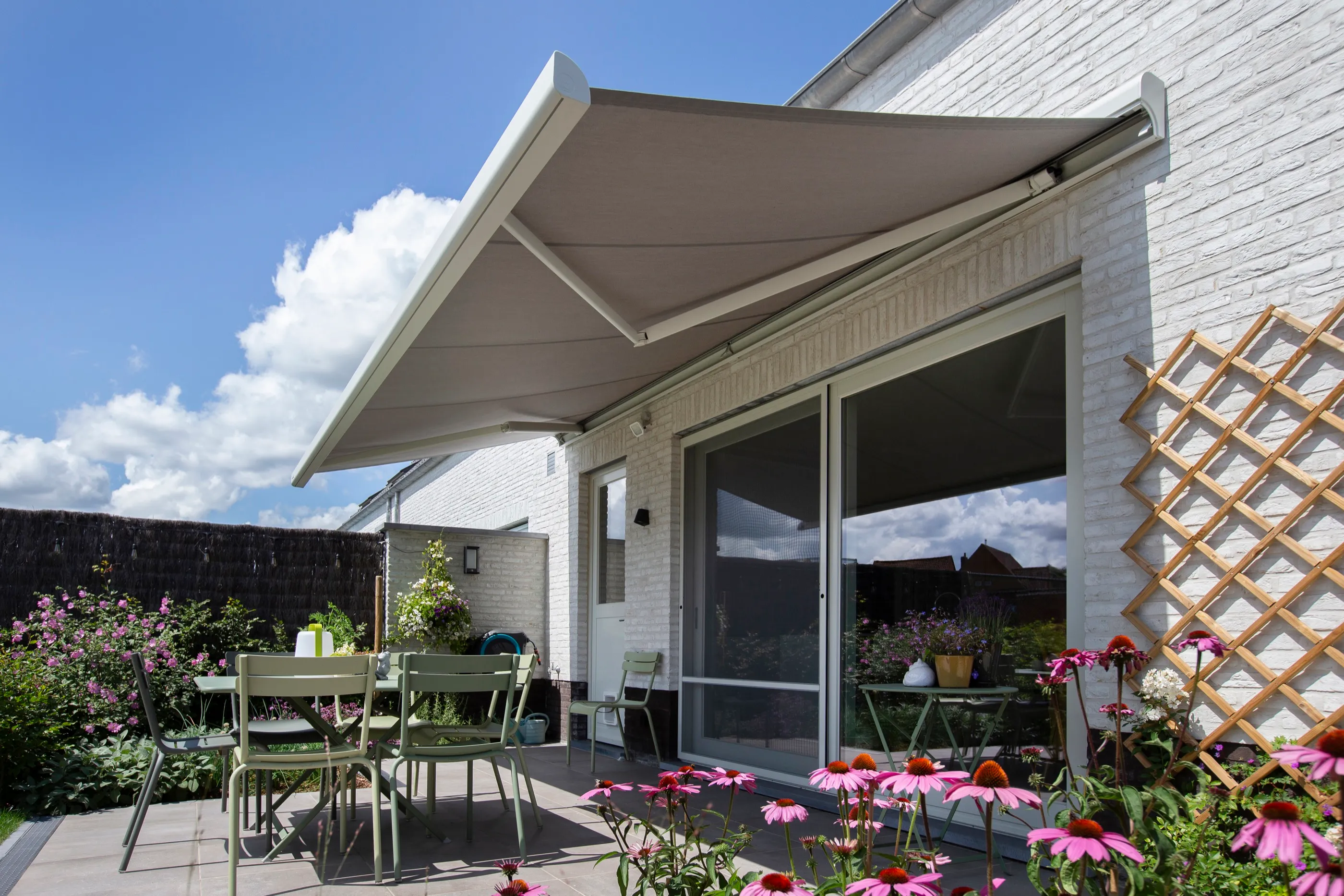 Ausgefahrene helle Markise über einer Gartenterrasse mit Blumen und Sitzplatz